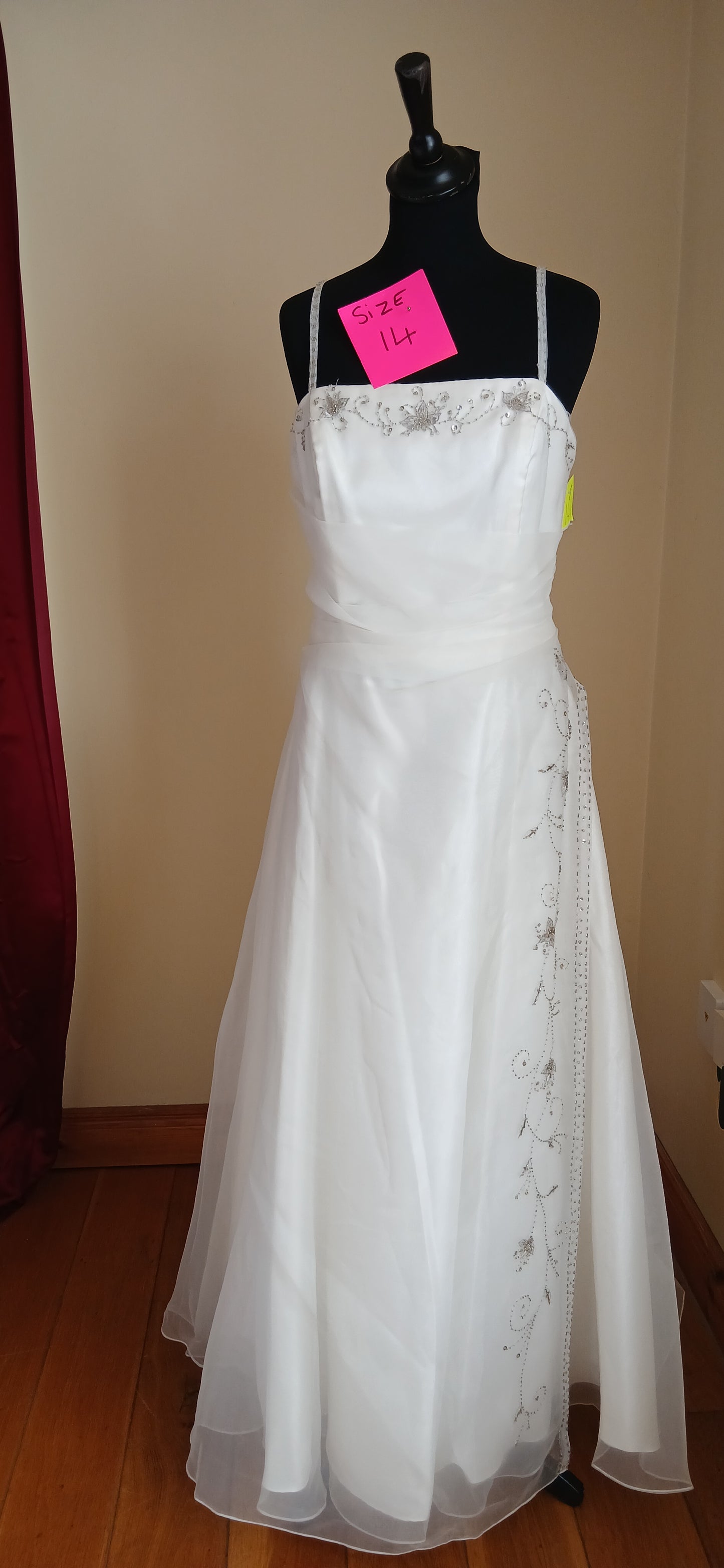 This exquisite size 14 ivory organza dress is a masterpiece, featuring delicate floral details at the bust and down the front to the hem.