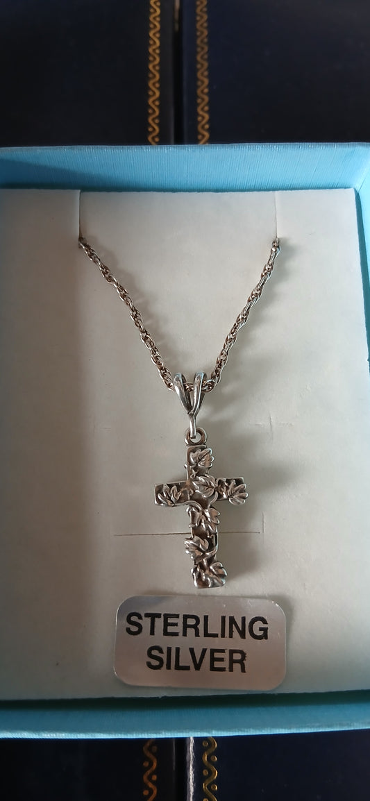 A sterling silver cross with vines design on a chain, displayed in a box with a 'STERLING SILVER' label.