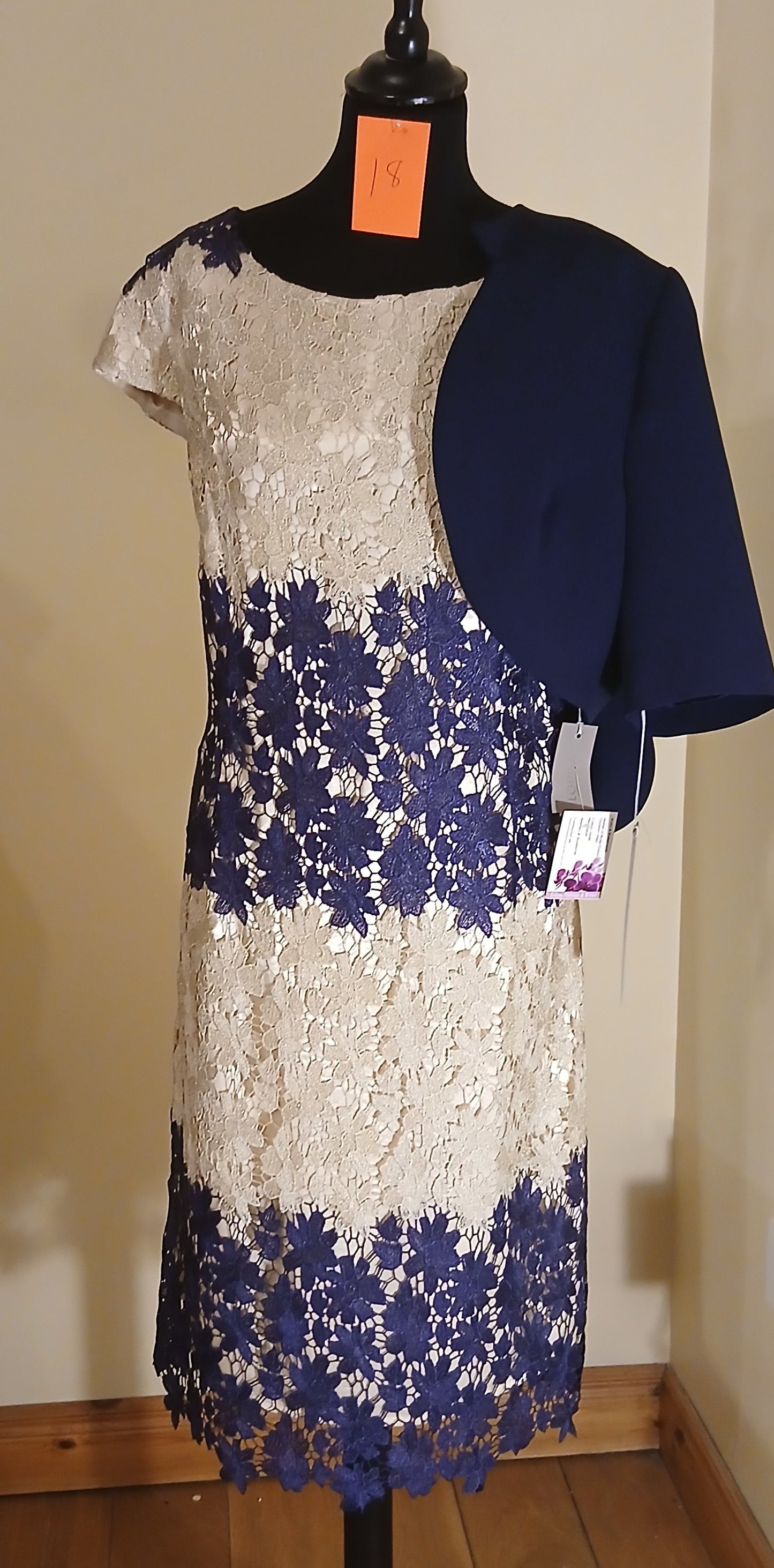 Make a lasting impression with our exquisite Mother of Bride and Groom outfit. This size 18 ensemble features a stunning gold and navy floral lace dress, perfectly complemented by a navy bolero jacket with delicate scalloped details. The dress exudes elegance and grace, while the bolero jacket adds a touch of sophistication. This outfit is a must-have for any special occasion, and the floral lace design ensures a timeless and memorable look.