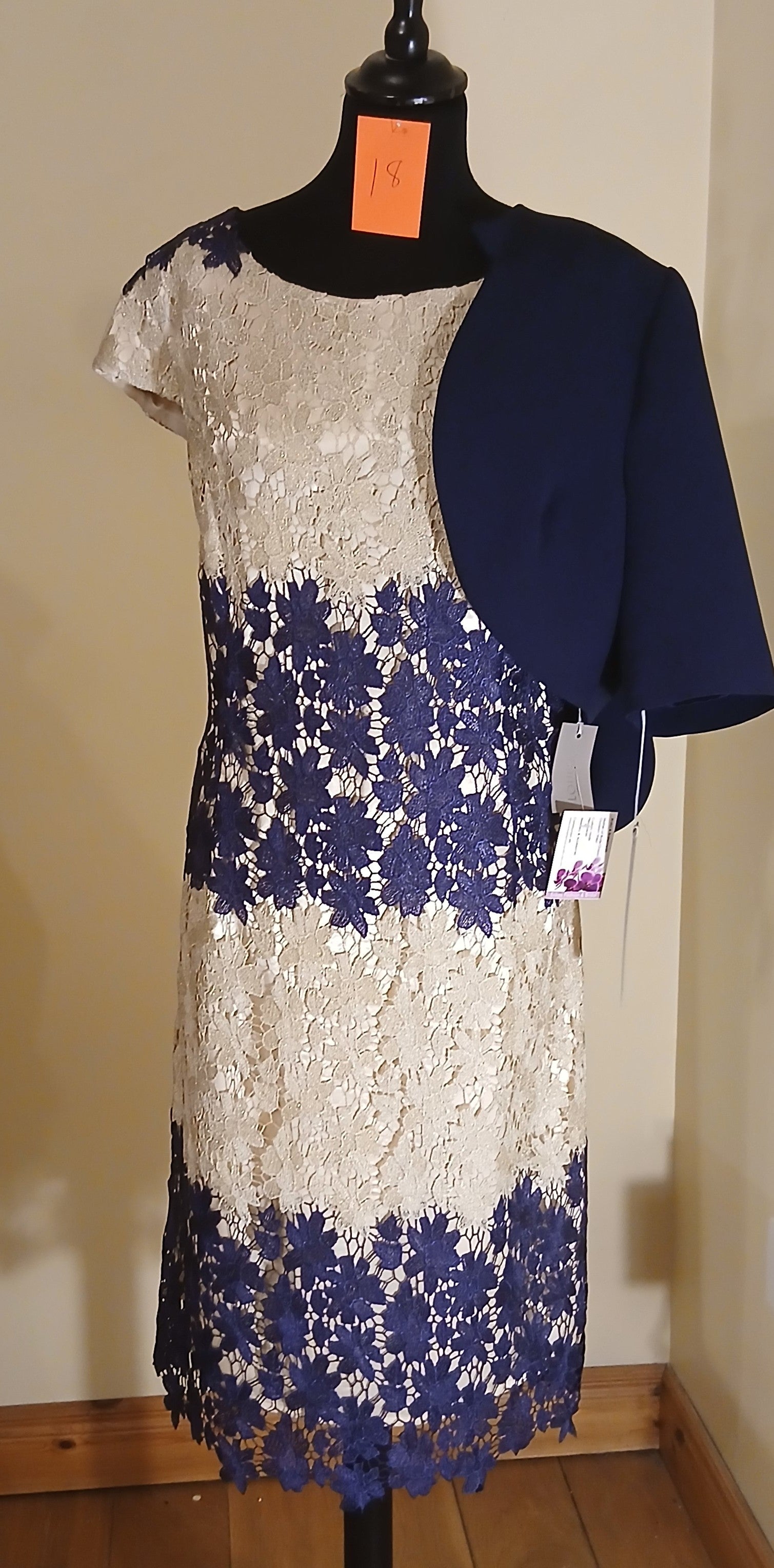 Make a lasting impression with our exquisite Mother of Bride and Groom outfit. This size 18 ensemble features a stunning gold and navy floral lace dress, perfectly complemented by a navy bolero jacket with delicate scalloped details. The dress exudes elegance and grace, while the bolero jacket adds a touch of sophistication. This outfit is a must-have for any special occasion, and the floral lace design ensures a timeless and memorable look.