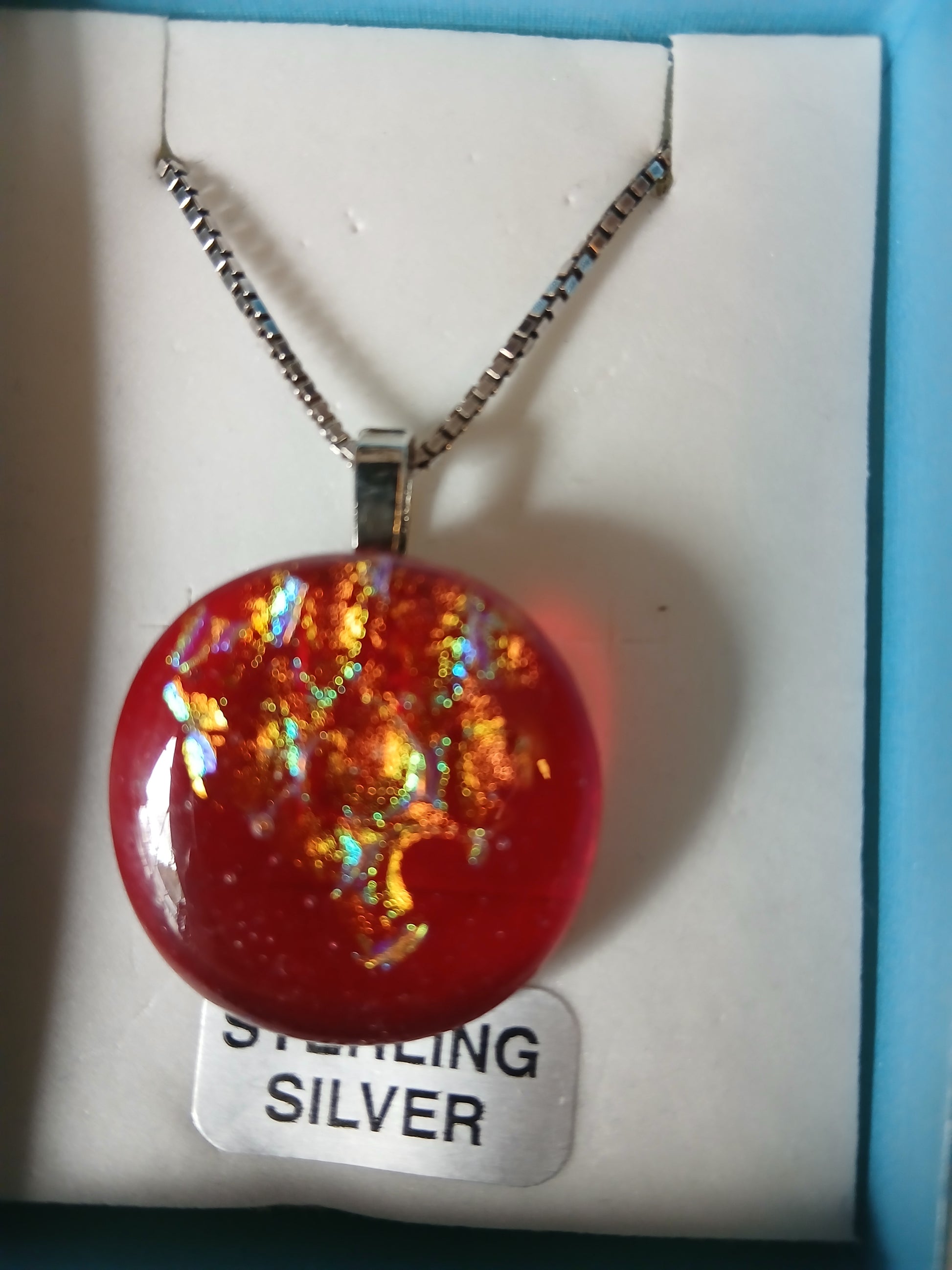 Main Description: "Ignite your style with this mesmerizing Fire Ice dichroic glass pendant that captures the essence of flickering flames frozen in time. This stunning handcrafted piece features a captivating blend of fiery red, molten gold, emerald green, and rich copper tones that shift and dance with every movement. The dichroic glass creates an enchanting play of light, making each viewing angle reveal new depths of color and brilliance.

Suspended on an elegant sterling silver chain, this one-of-a-kind